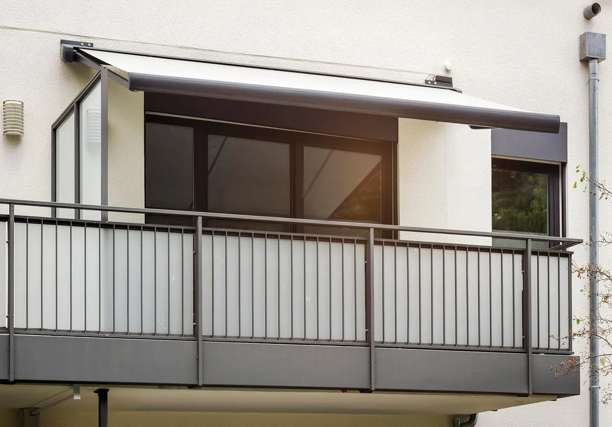 Store banne à coffre gris déployé au-dessus d'un balcon à garde-corps métallique sur une façade d'immeuble